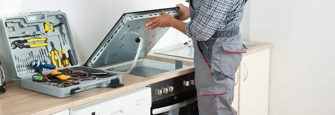 Cooktop repair technician lifting a built-in stovetop for service in South Bend, IN