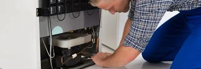 Refrigerator repair technician servicing the compressor and condenser area in South Bend, IN