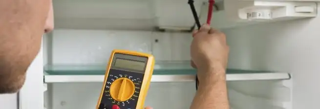 Refrigerator repair technician testing electrical components with a multimeter in South Bend, IN